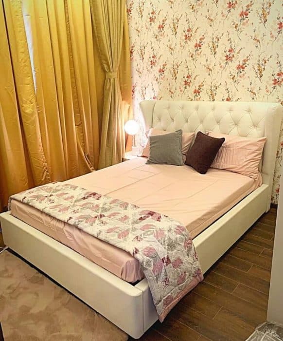 A-White-Upholstered-Double-Bed-with-a-High-Wingback-Button-Tufted-Headboard-Grey-Brown-Cushion-Bedsheet-Style-gives-a-charm-to-the-Bed-Setup. Design Detail Banner 0