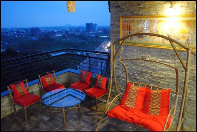 Balcony-having-a-City-View-Metal-Frame-Chair-with-Orange-Cushioned-Seating-2-Seater-Swing-Round-Coffee-Table-with-Glass-top. Swiper Content 0
