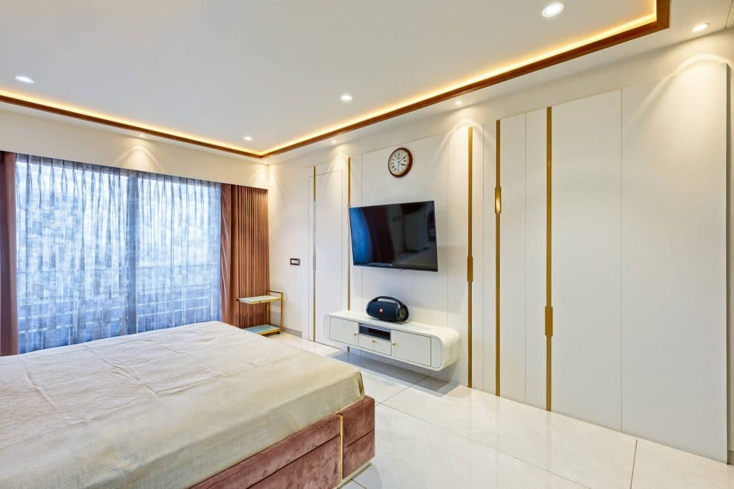 Bedroom-comprising-Wooden-Bed-Brown-Coloured-Cushioned-Headboard-highlighted-by-Golden-Stipes-Side-Tables-Wall-Lights-T.V.-Unit-Full-Height-Overlooking-Windows-adorned-with-Sheer-Dra-1 Design Detail Banner 2