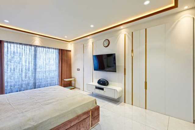 Bedroom-comprising-Wooden-Bed-Brown-Coloured-Cushioned-Headboard-highlighted-by-Golden-Stipes-Side-Tables-Wall-Lights-T.V.-Unit-Full-Height-Overlooking-Windows-adorned-with-Sheer-Dra-1 Swiper Content 2
