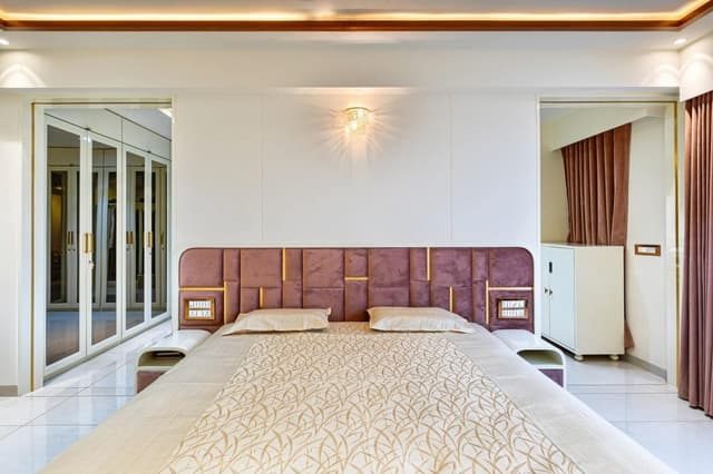 Bedroom-comprising-Wooden-Bed-Brown-Coloured-Cushioned-Headboard-highlighted-by-Golden-Stipes-Side-Tables-Wall-Lights-T.V.-Unit-Full-Height-Overlooking-Windows-adorned-with-Sheer-Drapes Swiper Content 1