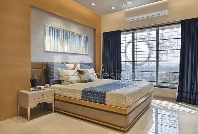 Bedroom-in-Light-Dark-shades-of-Cream-accommodating-Wooden-Bed-Side-Tables-with-a-Buddha-on-it-Cushioned-Headboard-Wall-Framed-Painting-on-the-Bed-Backwall-highlighted-with-Spot-Lights. Swiper Content 0