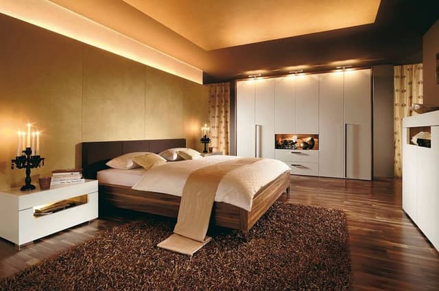 Bedroom-in-Rust-Brown-Theme-comprising-Wooden-Bed-Side-Tables-with-Table-Lamp-place-on-it-Rug-6-Door-Wooden-White-Coloured-Wardrobe. Swiper Content 0