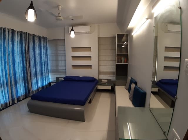 Bedroom-with-Wooden-Bed-having-Round-Edges-Attached-Side-Tables-Full-Height-Display-Shelves-on-one-Corner-Seating-Cushions-over-the-Drawers-1 Swiper Content 0