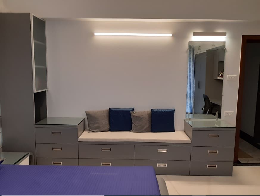 Bedroom-with-Wooden-Bed-having-Round-Edges-Attached-Side-Tables-Full-Height-Display-Shelves-on-one-Corner-Seating-Cushions-over-the-Drawers-3 Design Detail Banner 2