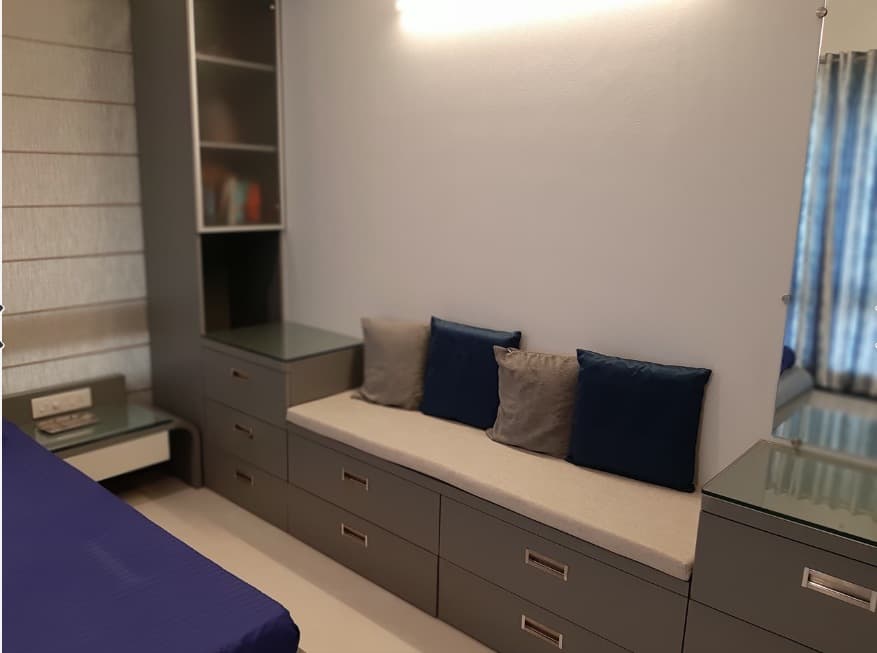 Bedroom-with-Wooden-Bed-having-Round-Edges-Attached-Side-Tables-Full-Height-Display-Shelves-on-one-Corner-Seating-Cushions-over-the-Drawers-4 Design Detail Banner 3