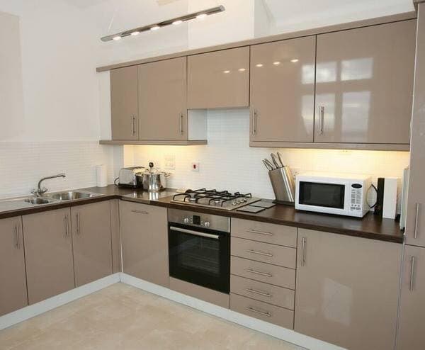 L-Shaped-Kitchen-in-Beige-Cabinets-Brown-Countertop-Hidden-Chimney-under-Cabinet-over-a-Built-in-Stove-Under-Cabinets-Lights-Suspended-Track-Spot-Lights L Shaped Kitchen