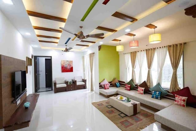 Living-Room-accommodating-C-Shaped-Low-Heighted-Sofa-with-Colourful-Cushions-Coffee-Table-placed-on-a-Rug-T.V.-Unit-Sofa-Chairs-with-attached-Storage-Unit-Hanging-Pendant-Lights. Swiper Content 0