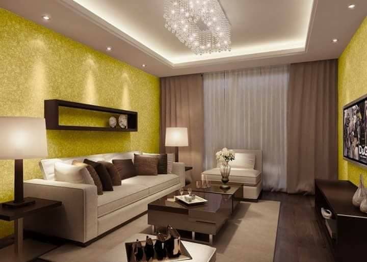 Living-Room-accommodating-Square-Armed-Sofa-Armless-Sofa-Chair-Wooden-Coffee-Table-placed-on-a-Rug-Box-Wall-Shelves-on-Wall-with-Dense-Printed-Yellow-Wallpaper-Table-Lamps-T.V.-Unit. Design Detail Banner 0