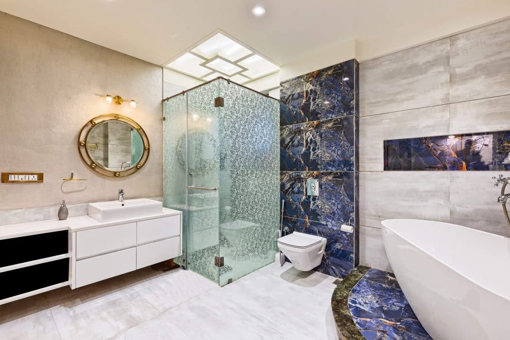 Luxurious-Bathroom-finished-with-Highlighting-Bluish-Marble-Tiles-with-Grey-Tiles-accommodating-Dry-Area-including-WC-Bathtub-Table-Top-Wash-Basin-with-Wooden-Cabinets-below-Round-Mirror Design Detail Banner 0