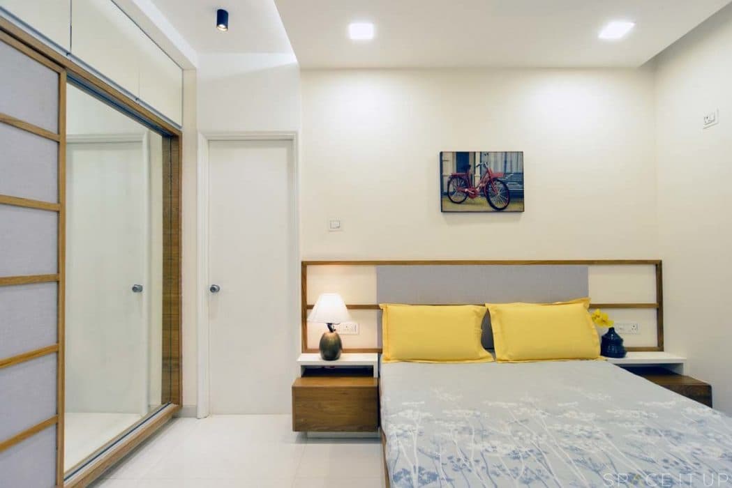 Minimalist-Bedroom-designed-with-Wooden-Bed-Side-Tables-with-Table-Lamps-placed-on-it-Wall-Painting-on-Bed-Backwall Design Detail Banner 0