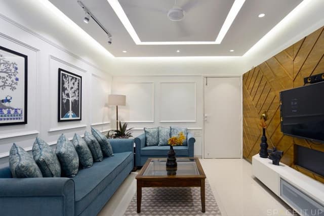 Modern-Living-Room-designed-with-Blue-Coloured-Roll-Arm-Sofa-Set-Wooden-Glass-Top-Coffee-Table-placed-on-a-Rug-Corner-Side-Table-with-Table-Lamp-Wall-mounted-T.V.-Unit-1 Swiper Content 0