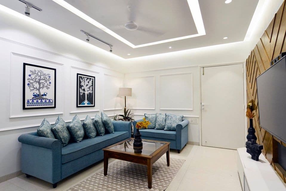 Modern-Living-Room-designed-with-Blue-Coloured-Roll-Arm-Sofa-Set-Wooden-Glass-Top-Coffee-Table-placed-on-a-Rug-Corner-Side-Table-with-Table-Lamp-Wall-mounted-T.V.-Unit-2 Design Detail Banner 1