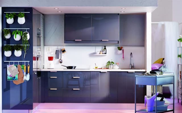 Modern-Single-Wall-Modular-Kitchen-with-Upper-Lower-Cabinets-in-Navy-Blue-Colour-Glossy-Finish.-It-comprise-of-Tall-Storage-Units-with-Built-in-Ovens-Hanging-Indoor-Plants-Hooks-for-Hangin Swiper Content 0