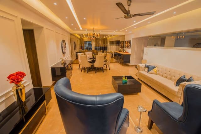 This-Luxurious-Living-Room-having-a-Cream-Chesterfield-Sofa-two-High-Wingback-Blue-chairs.-Black-Glossy-Cubicle-Center-Table-with-the-Storage-is-Functionally-Supporting-the-Seating-Area.-2 Swiper Content 1