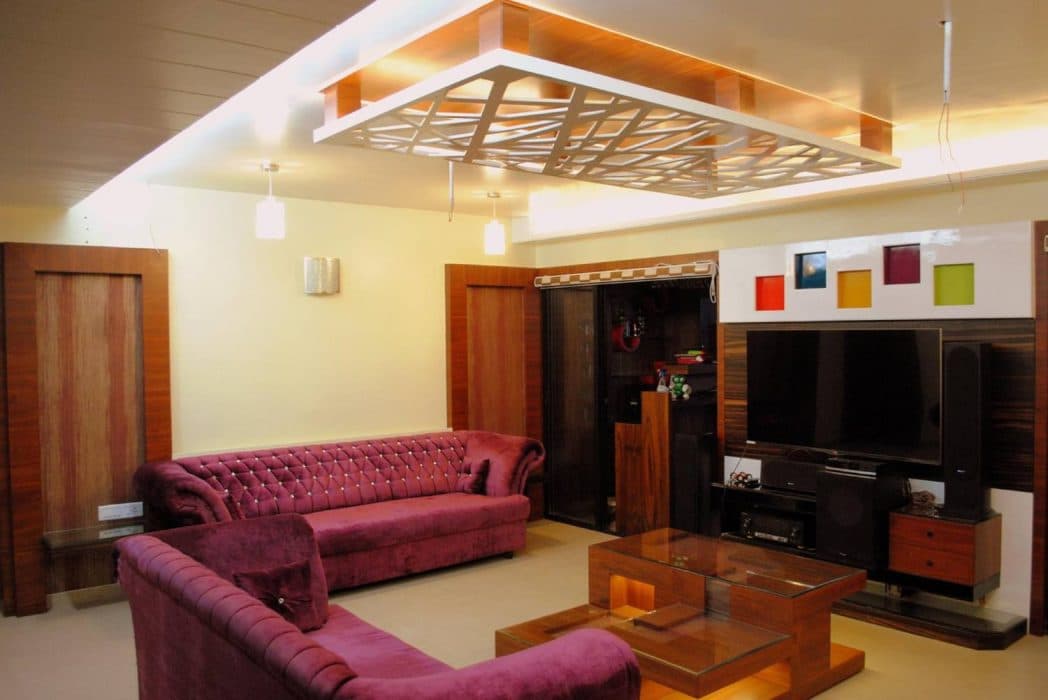 Tuxedo-Style-Dark-Purple-Colour-Sofa-is-making-this-Living-Room-more-Luxurious.-A-Multilevel-Modular-Polished-Finish-Wooden-Coffee-Table-with-Glass-top-Niches-highlighted-with-Spot-Lights Design Detail Banner 0