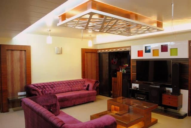 Tuxedo-Style-Dark-Purple-Colour-Sofa-is-making-this-Living-Room-more-Luxurious.-A-Multilevel-Modular-Polished-Finish-Wooden-Coffee-Table-with-Glass-top-Niches-highlighted-with-Spot-Lights Swiper Content 0