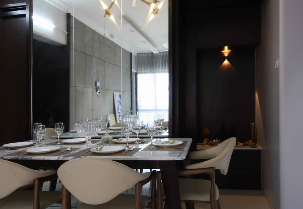 A dark frame marble topped dining table with elegant glassware and dining chairs having crème colour covering. A dark frame marble topped dining table with elegant glassware and dining chairs having crème colour covering.